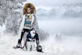 Beautiful blonde woman, standing on snow and holding Husky dogs view of mountains and snow.