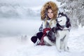 Beautiful blonde woman, standing on snow and holding Husky dogs view of mountains and snow.