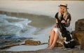 Beautiful blonde woman in straw hat sitting on a rock and petting the good dog. The same color. Thai beach. Morning walk Royalty Free Stock Photo