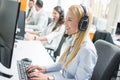 Beautiful blonde woman telephone operator talking with customer in call center.