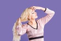 Beautiful blonde woman touches her long hair with her hands on purple background with copy space Royalty Free Stock Photo