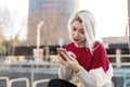 Beautiful blonde woman using her mobile phone while sitting on a bench in the street Royalty Free Stock Photo