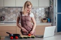 A beautiful blonde woman using laptop computer in the kitchen and cut vegetables for salad cooking and watching a movie Royalty Free Stock Photo