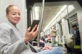 Beautiful blonde woman using smart phone while traveling by metro public transport.