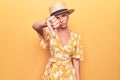 Beautiful blonde woman on vacation wearing summer hat and dress over yellow background looking unhappy and angry showing rejection Royalty Free Stock Photo