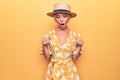 Beautiful blonde woman on vacation wearing summer hat and dress over yellow background Pointing down with fingers showing Royalty Free Stock Photo