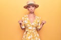 Beautiful blonde woman on vacation wearing summer hat and dress over yellow background Pointing down looking sad and upset, Royalty Free Stock Photo