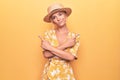 Beautiful blonde woman on vacation wearing summer hat and dress over yellow background Pointing to both sides with fingers,