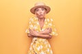 Beautiful blonde woman on vacation wearing summer hat and dress over yellow background shaking and freezing for winter cold with Royalty Free Stock Photo