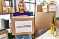 Beautiful blonde woman volunteer holding donations box in shock face, looking skeptical and sarcastic, surprised with open mouth Royalty Free Stock Photo