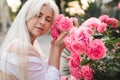 Beautiful blonde woman wear stylish white top with corset posing over blooming flower roses outdoors close up. Royalty Free Stock Photo