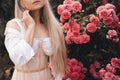 Beautiful blonde woman wear stylish white top with corset posing over blooming flower roses outdoors close up. Royalty Free Stock Photo