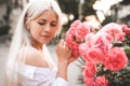 Beautiful blonde woman wear stylish white top with corset posing over blooming flower roses outdoors close up. Royalty Free Stock Photo