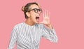 Beautiful blonde woman wearing business shirt and glasses shouting and screaming loud to side with hand on mouth