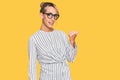 Beautiful blonde woman wearing business shirt and glasses smiling with happy face looking and pointing to the side with thumb up Royalty Free Stock Photo