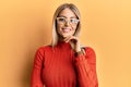 Beautiful blonde woman wearing casual clothes and glasses smiling looking confident at the camera with crossed arms and hand on Royalty Free Stock Photo