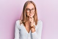 Beautiful blonde woman wearing casual clothes and glasses smiling looking confident at the camera with crossed arms and hand on Royalty Free Stock Photo