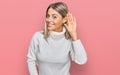 Beautiful blonde woman wearing casual turtleneck sweater smiling with hand over ear listening an hearing to rumor or gossip Royalty Free Stock Photo