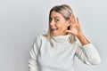 Beautiful blonde woman wearing casual turtleneck sweater smiling with hand over ear listening and hearing to rumor or gossip Royalty Free Stock Photo