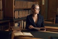 Female model sitting at desk and reading book at library Royalty Free Stock Photo