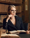 Female model sitting at desk and reading book at library Royalty Free Stock Photo