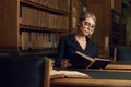 Female model sitting at desk and reading book at library Royalty Free Stock Photo