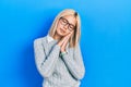 Beautiful blonde woman wearing glasses sleeping tired dreaming and posing with hands together while smiling with closed eyes Royalty Free Stock Photo