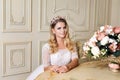 Beautiful blonde woman wearing gorgeous dress and crystal crown posing in luxury classic apartment. Royalty Free Stock Photo