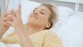 Young blonde woman typing on phone while lying on a bed.