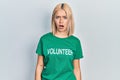Beautiful blonde woman wearing volunteer t shirt in shock face, looking skeptical and sarcastic, surprised with open mouth
