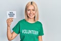 Beautiful blonde woman wearing volunteer t shirt showing we need you banner looking positive and happy standing and smiling with a Royalty Free Stock Photo