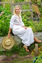 Beautiful blonde woman in white dress sitting outside in garden