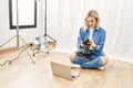 Beautiful blonde woman working as professional photographer at photography studio sitting on the floor checking photos on computer Royalty Free Stock Photo