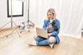Beautiful blonde woman working as professional photographer at photography studio sitting on the floor checking photos on computer Royalty Free Stock Photo