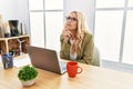 Beautiful blonde woman working at the office with laptop with hand on chin thinking about question, pensive expression Royalty Free Stock Photo