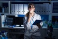 Beautiful blonde woman working at scientist laboratory late at night thinking concentrated about doubt with finger on chin and Royalty Free Stock Photo