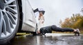 Charming young woman watching how man fixing car wheel. Royalty Free Stock Photo