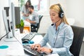 Beautiful blonde young business woman with headset using computer at office. Royalty Free Stock Photo