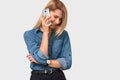 Beautiful blonde young female talking on cell phone to her boyfriend, looking cheerful and happy on white studio background Royalty Free Stock Photo
