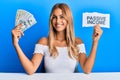 Beautiful blonde young woman holding dollars and passive income text smiling with a happy and cool smile on face