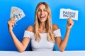Beautiful blonde young woman holding dollars and passive income text smiling and laughing hard out loud because funny crazy joke