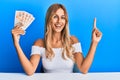 Beautiful blonde young woman holding 10 united kingdom pounds banknotes smiling with an idea or question pointing finger with
