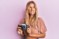 Beautiful blonde young woman holding vintage camera angry and mad screaming frustrated and furious, shouting with anger looking up Royalty Free Stock Photo