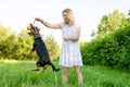 A beautiful blonde young woman holds a ball in her hand for which a dog clung to in a jump