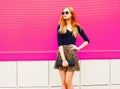 Beautiful blonde young woman in leopard skirt, sunglasses with handbag clutch posing on colorful pink Royalty Free Stock Photo