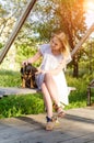 A beautiful blonde young woman in a light dress with her cute dog is sitting on a park bench. Vertical view Royalty Free Stock Photo