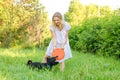 A beautiful blonde young woman in a light dress is holding a flying disc that a cute dog clung to