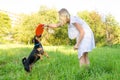 A beautiful blonde young woman in a light dress is holding a frisbee that a cute dog clung to