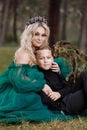 A beautiful blonde young woman in a long green dress and a diadem on her head with stylish young son in the forest. girl and boy Royalty Free Stock Photo