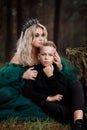 A beautiful blonde young woman in a long green dress and a diadem on her head with stylish young son in the forest. girl Royalty Free Stock Photo